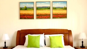A hotel room with a large bed, two bedside lamps, and three landscape paintings on the wall.