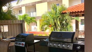An outdoor patio with two barbecue grills, a hand washing station, and a view of a building with balconies.