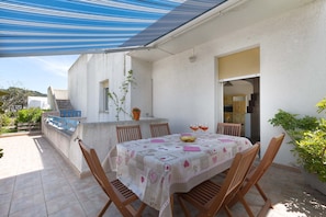 Un patio exterior con una mesa dispuesta para cuatro personas, rodeado de sillas de madera.