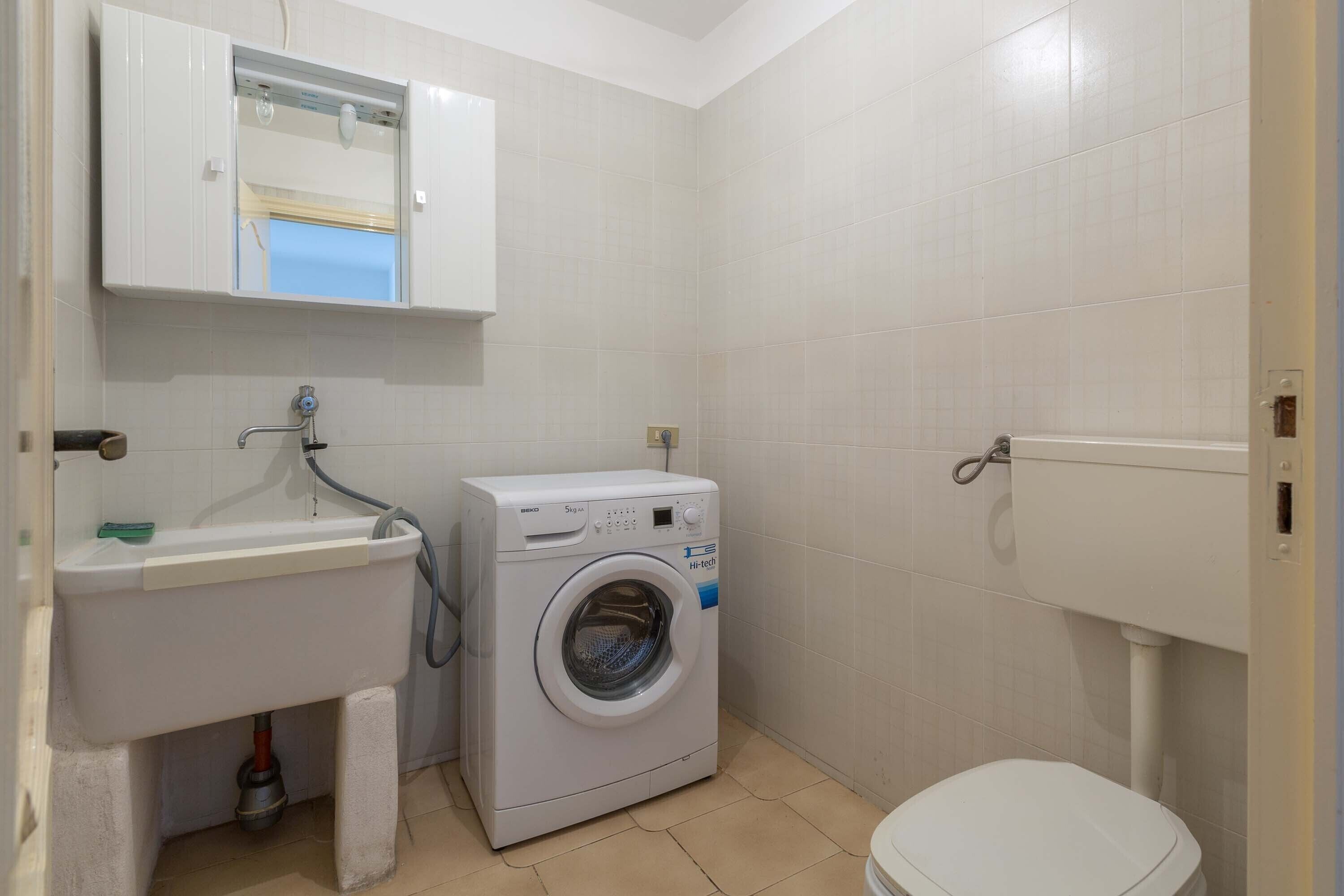 Een kleine badkamer met een wasmachine, een wastafel en een toilet.
