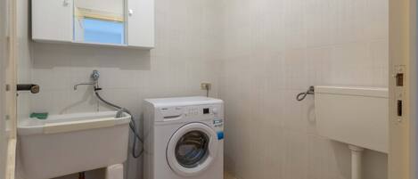 Een kleine badkamer met een wasmachine, een wastafel en een toilet.