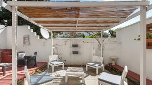 A covered patio area with white furniture, a table, and a pergola with a wooden roof. - 2328 Mamma Teresa (Castro)