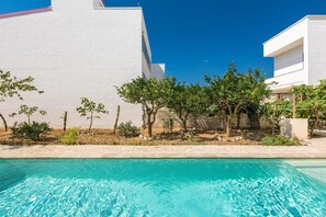 A swimming pool with clear blue water, surrounded by a white building and trees.