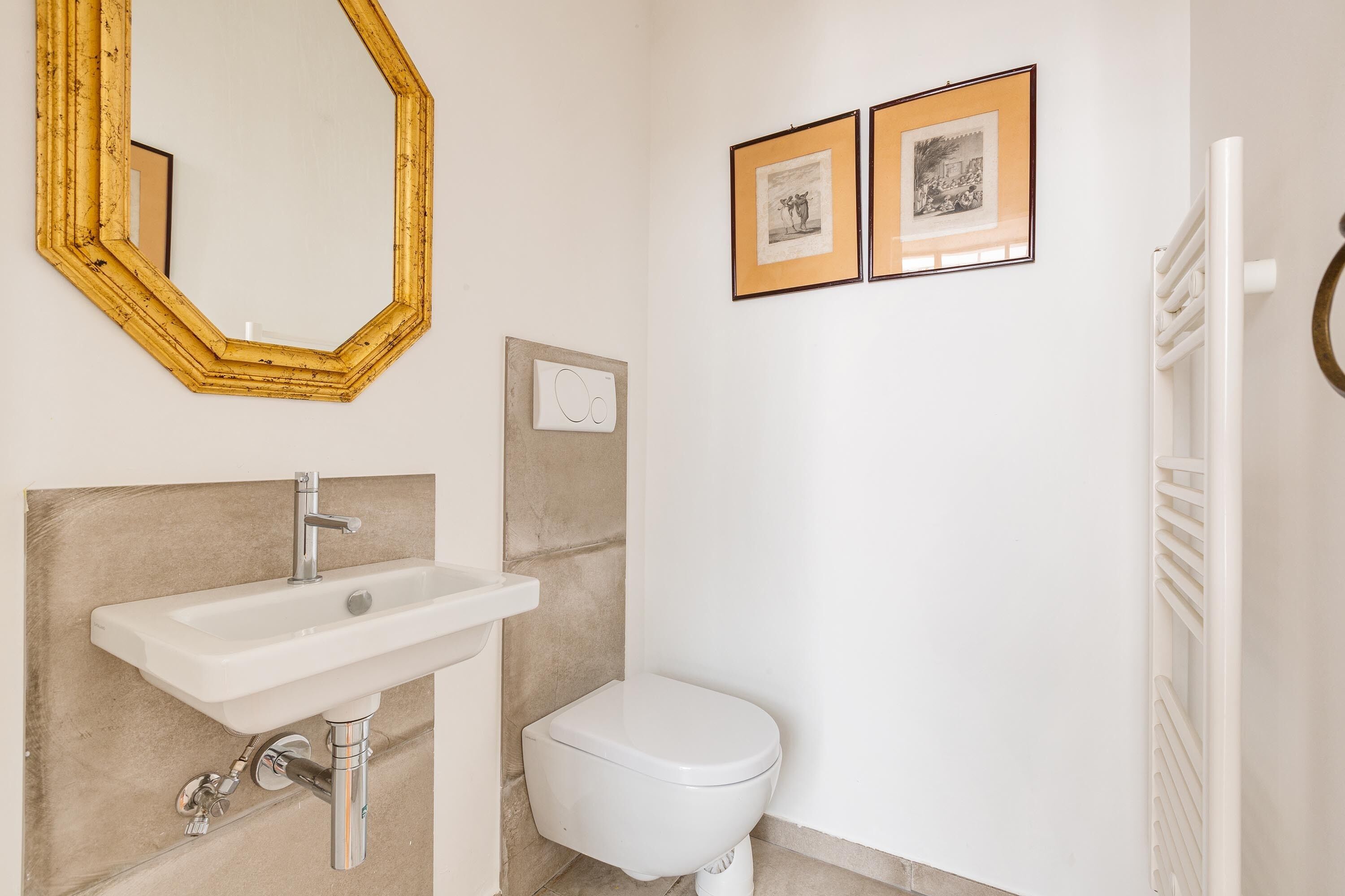 Een badkamer met een witte wastafel, een toilet, een spiegel en twee ingekaderde foto’s aan de muur.