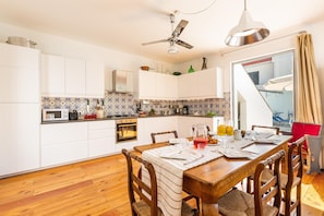 A modern kitchen with white cabinets, a wooden dining table, and a ceiling fan.