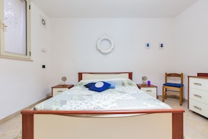 Une chambre à coucher comprenant un lit, des tables de chevet, une chaise en bois, une commode et un luminaire fixé au mur.