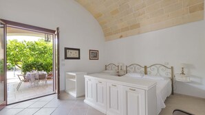 A bedroom with a bed, a bedside table, a chair, and a view of an outdoor patio with a table and chairs. - 3005 Dimora Donn`anna - Mono 1 by Barbarhouse (Ortelle)
