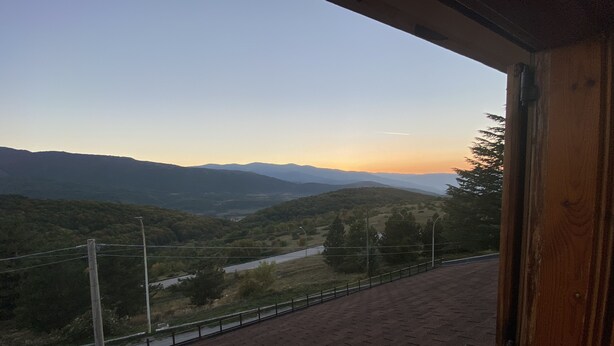 Vista da un balcone su una valle con un fiume e montagne in lontananza.