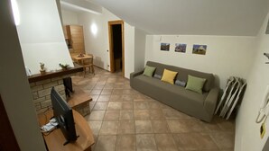 Un soggiorno con divano, televisione e zona pranzo con tavolo e sedie.