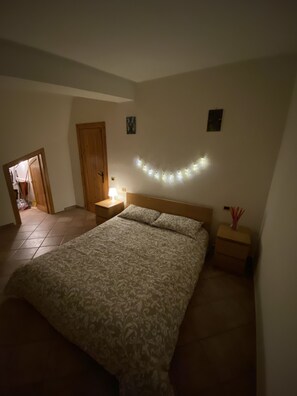 A bedroom with a bed, nightstands, a wall-mounted light, and a door.