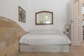 A bedroom with a bed, a bedside table, a lamp, and a mirror on the wall.