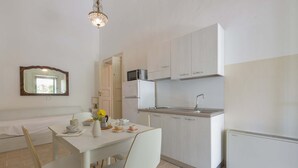 Una cocina moderna con armarios blancos, microondas y horno empotrado. Hay una mesa de comedor con sillas y un florero con flores.