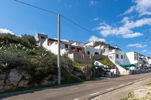 Una carretera costera con edificios blancos, algunos con balcones, y un cielo azul despejado.