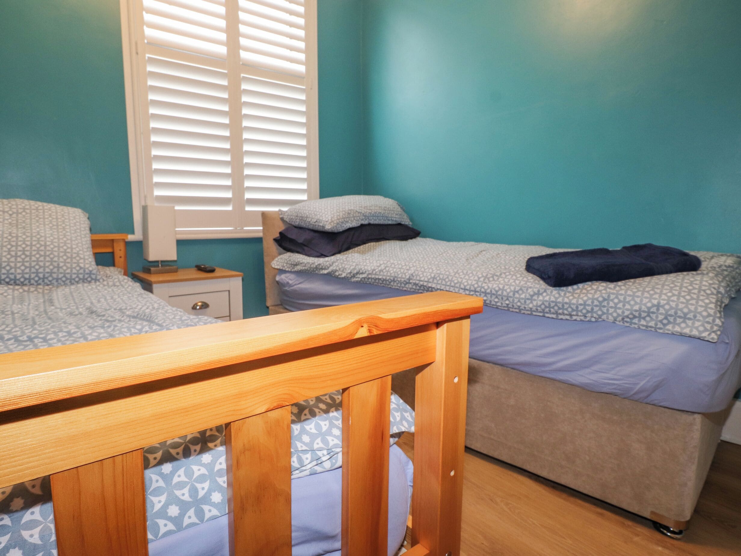 Un dormitorio con dos camas, cabecera de madera, mesita de noche y ventana con persianas.