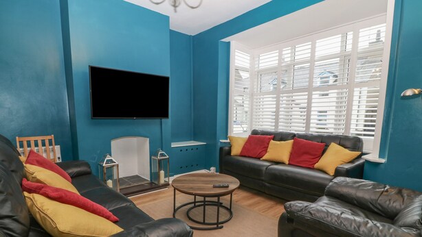 Un salon aux murs bleus, avec un canapé en cuir noir, une table basse en bois et un téléviseur à écran plat fixé au mur.