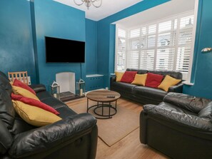 A living room with blue walls, a black leather sofa, a wooden coffee table, and a flat-screen TV mounted on the wall. - Glanffrwd - Nefyn (Pwllheli)