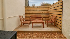 Une terrasse en bois avec une table et des chaises, entourée d’une clôture en bois et d’un mur blanc.