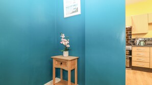 Un couloir aux murs de couleur turquoise, un plancher en bois, une petite table en bois sur laquelle est posée une orchidée en pot, et un tableau encadré accroché au mur.