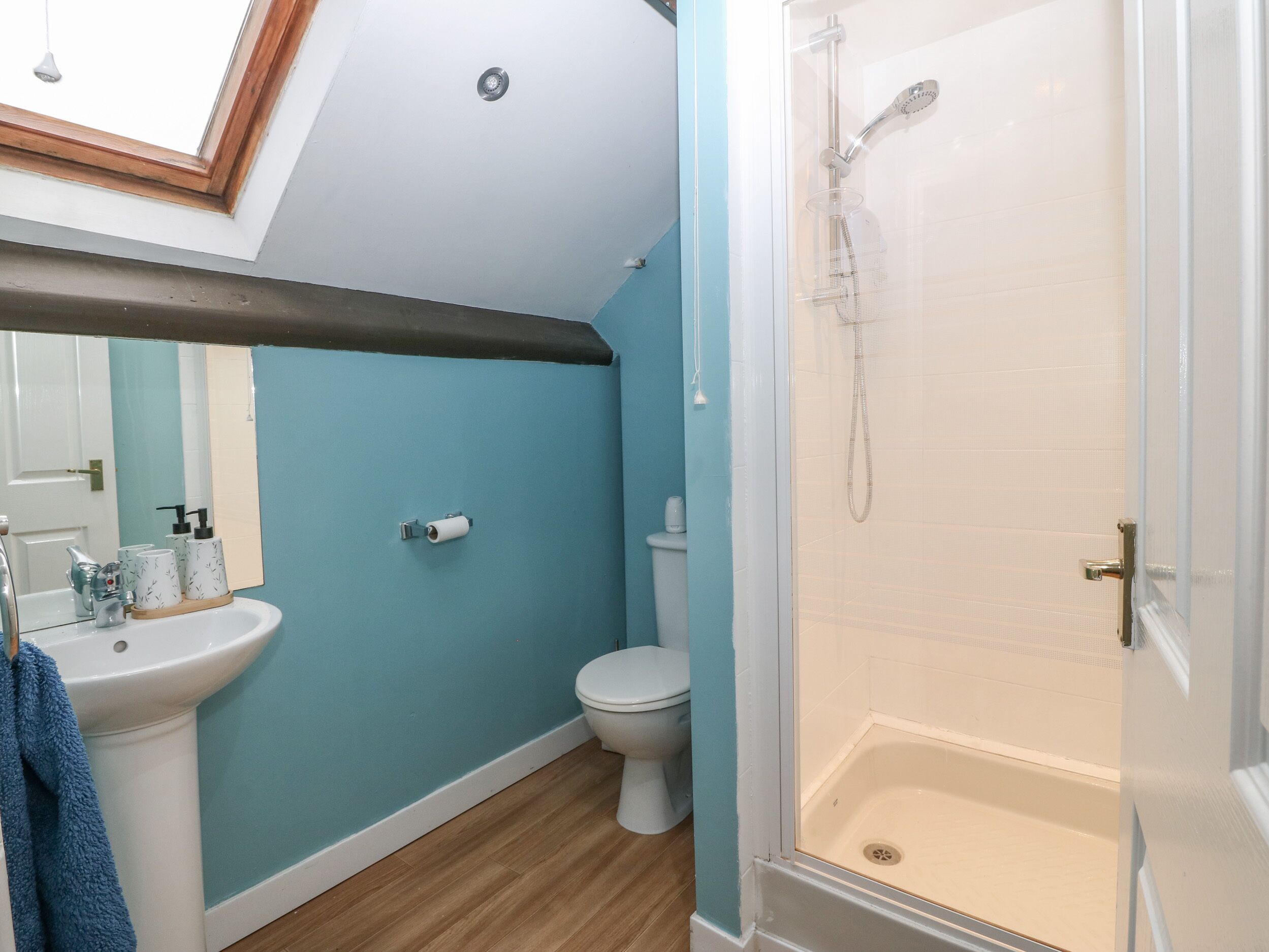 A bathroom with a blue wall, a white sink, a toilet, and a glass-enclosed shower.