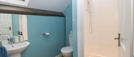 A bathroom with a blue wall, a white sink, a toilet, and a glass-enclosed shower.