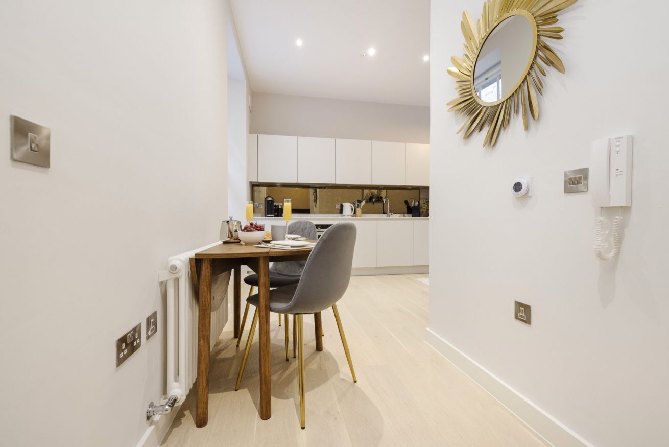 A modern kitchen with white cabinets, a dining table with chairs, and a gold-framed mirror on the wall.