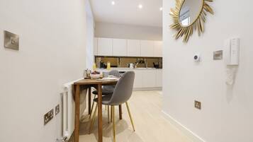 A modern kitchen with white cabinets, a dining table with chairs, and a gold-framed mirror on the wall.