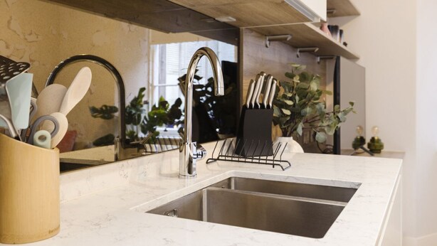 A modern kitchen with a stainless steel sink, a wooden countertop, and a mirror above the sink.