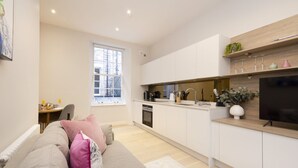 A modern kitchen with white cabinets, a wooden countertop, and a built-in oven. There is a dining area with a table and chairs, and a large window providing natural light.