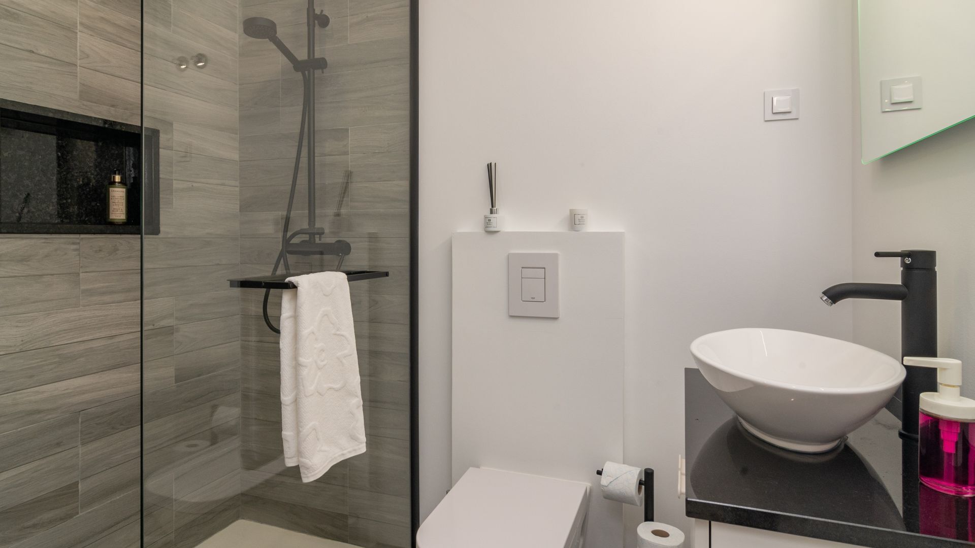 Une salle de bain moderne avec une douche à parois de verre, un lavabo blanc doté d’un grand bac et un robinet noir.