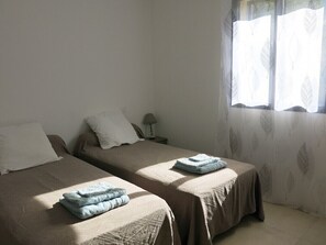 A room with two beds, each with a folded towel, a bedside table with a lamp, and a window with sheer curtains. - Fior d'alivu: New House with a Private Pool in the Countryside (Urtaca)
