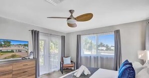 A hotel room with a bed, a ceiling fan, a TV, a desk, and a window with curtains.