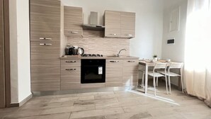 Une cuisine moderne avec des meubles en bois, un four encastré et un coin repas comprenant une table et des chaises blanches.