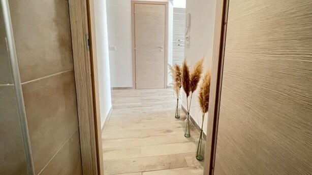 Un couloir doté d’un plancher en bois, une porte au fond et des herbes de la pampa disposées dans des vases.