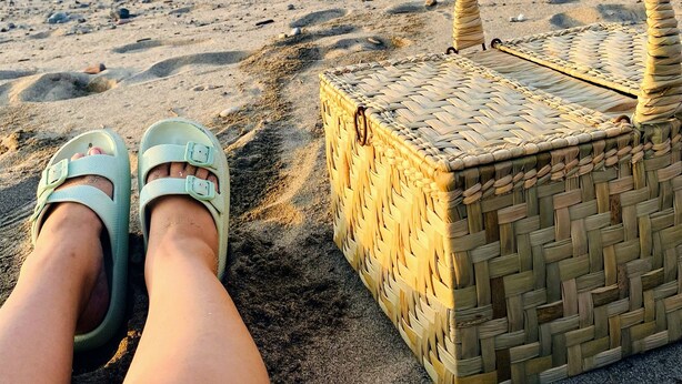 En strandscene med en fletkurv og sandaler på stranden.