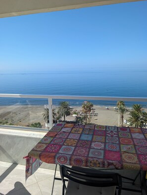 A balcony with a table covered in a colorful tablecloth, overlooking a beach with palm trees and a clear blue sky. - Algarrobo Costa luxury apartment POMELO , seafront, 6 pers, pool, sandy beach (Algarrobo)