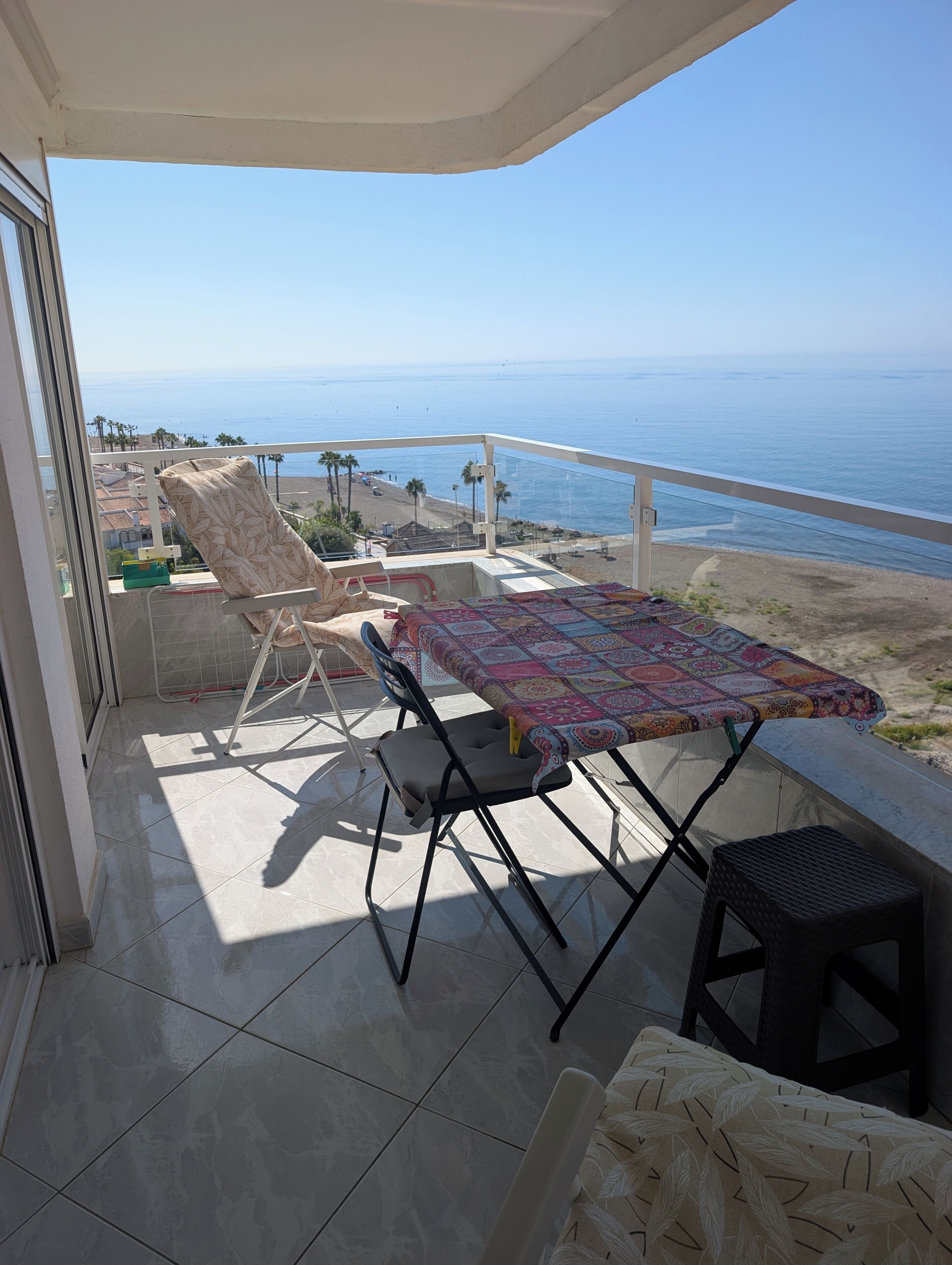 Un balcon avec une table et des chaises, donnant sur une plage et l’océan.