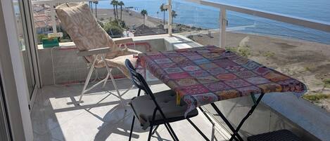 Un balcon avec une table et des chaises, donnant sur une plage et l’océan.