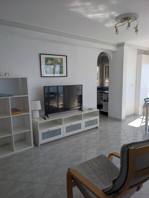 A living room with a flat-screen TV, white shelving, a framed picture, and a wooden chair. - Algarrobo Costa luxury apartment POMELO , seafront, 6 pers, pool, sandy beach (Algarrobo)
