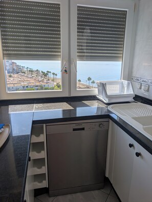 A kitchen with a dishwasher, a sink, and a window with blinds. - Algarrobo Costa luxury apartment POMELO , seafront, 6 pers, pool, sandy beach (Algarrobo)