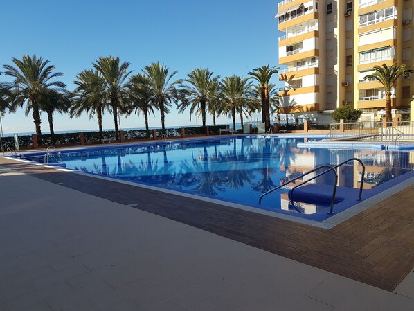 A swimming pool with clear blue water, surrounded by palm trees and a high-rise building in the background. - Algarrobo Costa luxury apartment POMELO , seafront, 6 pers, pool, sandy beach (Algarrobo)