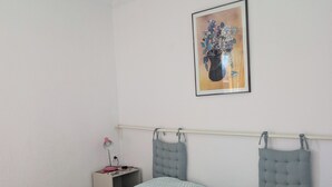 A bedroom with two beds, a nightstand, a lamp, and a framed floral artwork on the wall.