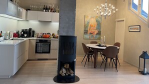 A modern kitchen with a central wood-burning stove, a dining area with a chandelier, and a painting on the wall. - Exclusive & Elegant Frogner Apartment in the Heart of Oslo (Oslo)