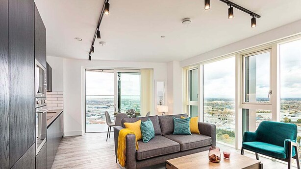 Ein modernes Wohnzimmer mit grauem Sofa, einem Couchtisch und Blick auf die Stadt durch große Fenster.