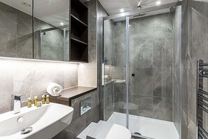 Et moderne badeværelse med et glasafskærmet brusebad, en hvid vask og en underskab med toiletartikler.