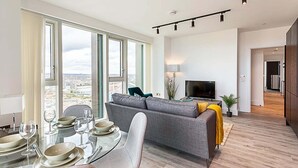 Ein modernes Wohnzimmer mit Sofa, Fernseher und Essbereich mit Tisch für vier Personen.