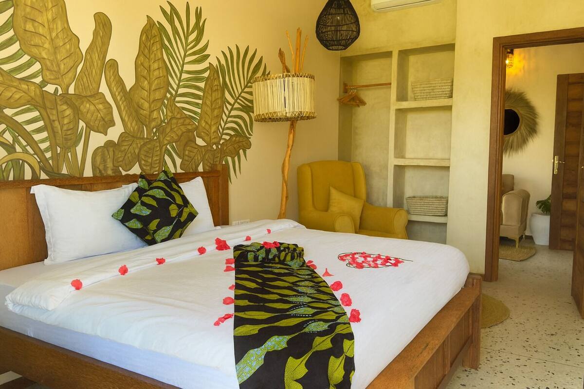 A bed with white linens, a patterned throw, and red rose petals.