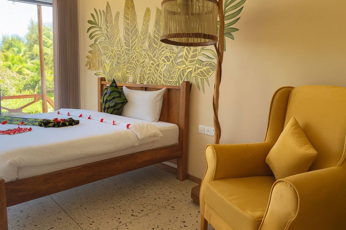 A room with a bed, a yellow armchair, a wooden headboard, a wall mural, and a hanging light fixture.