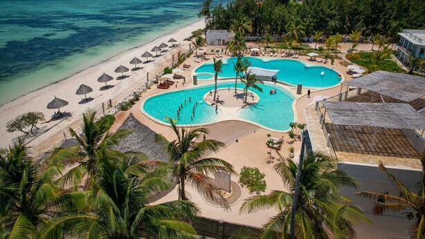 Et resort med stor swimmingpool, strand og palmer.