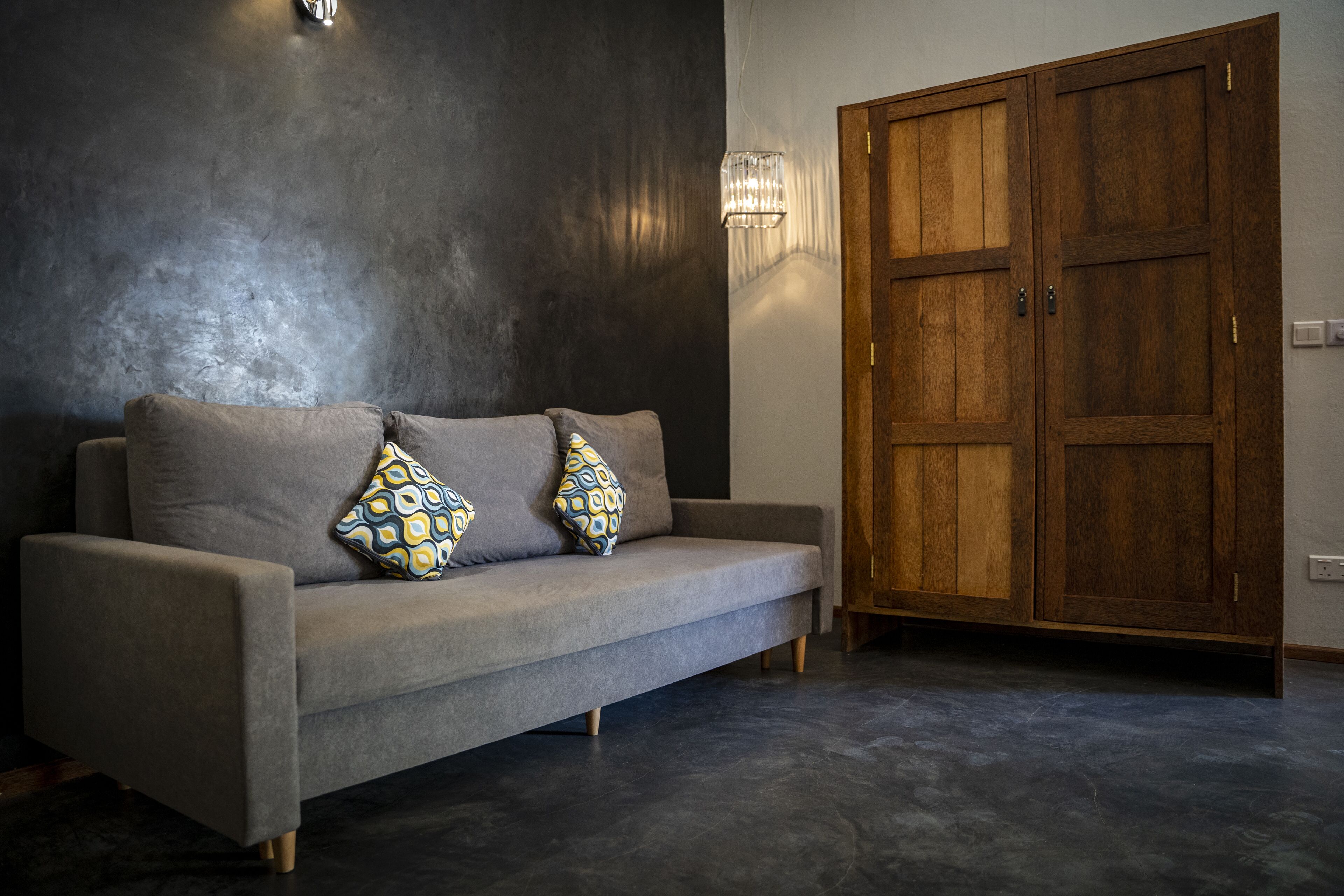 A modern living room with a grey sofa, patterned cushions, a wooden wardrobe, and a textured wall.