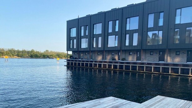 Moderni rakennus, jossa on tasakatto ja suuret ikkunat, ja joka sijaitsee rauhallisen vesistön äärellä.